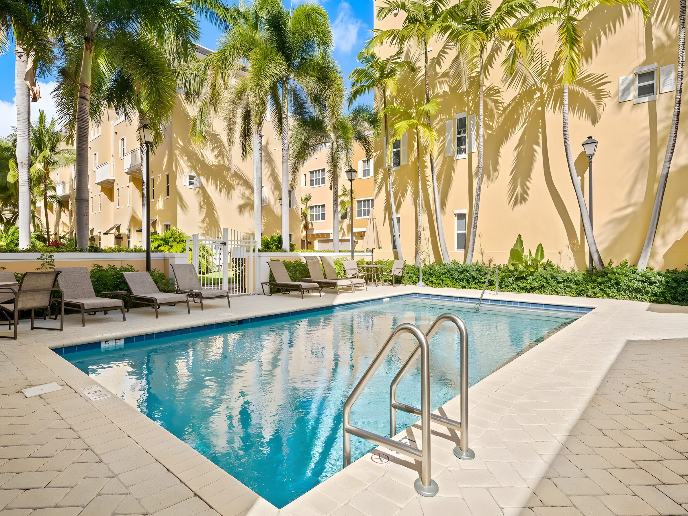 The community pool with lounge chairs, palms and the yellow townhomes behind.