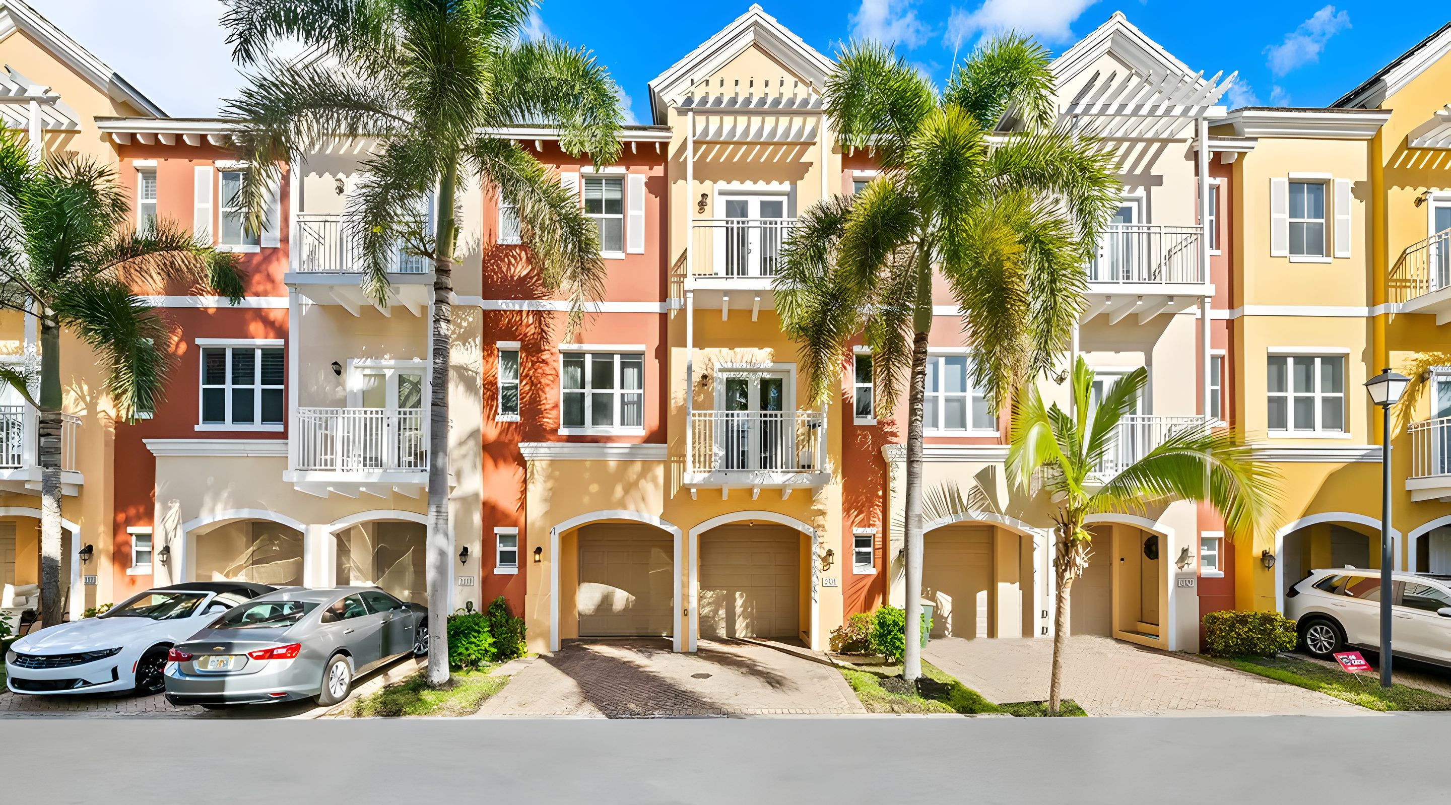 A row of ochre, coral and yellow three-storey townhomes with white balconies, garages and palms.
